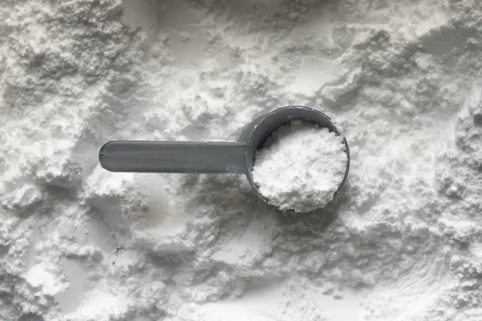 A gray scoop holding white supplement powder resting in a bed of more powder, evoking glutamine, the widely sold supplement-powder amino acid, in the glutamine versus glutathione comparison.
