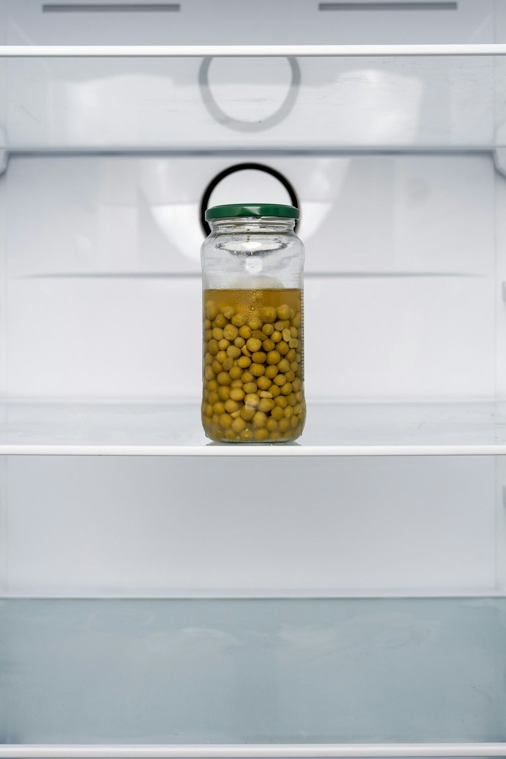 A single unlabeled glass jar on the middle shelf of an otherwise empty refrigerator