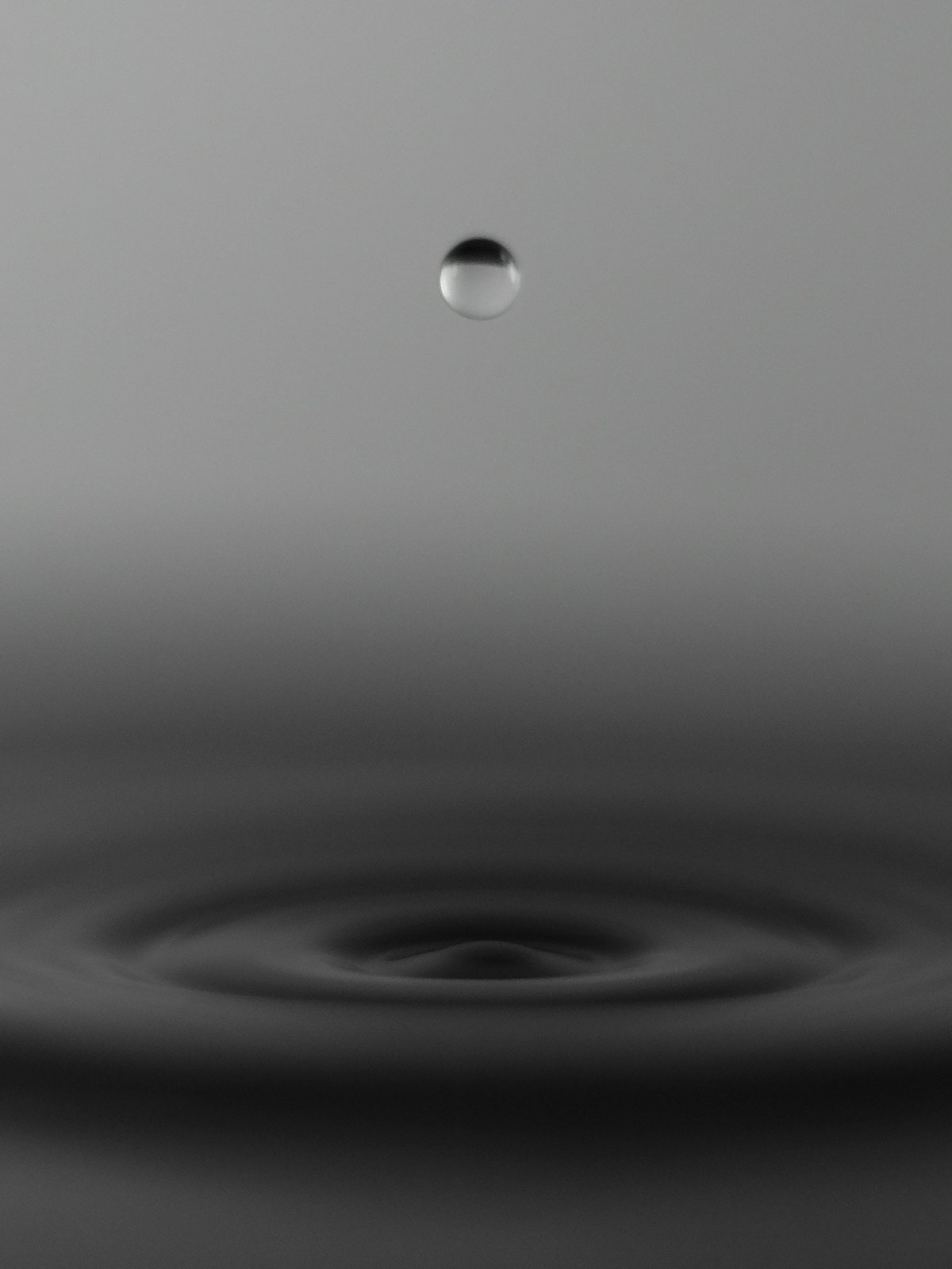A single water droplet suspended above fading concentric ripples, a visual analogy for tirzepatide clearing the system