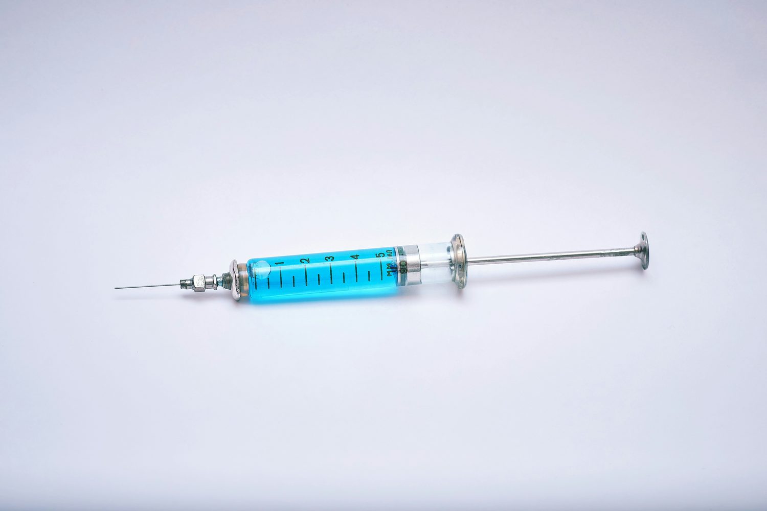 A medical syringe filled with blue liquid on a light background