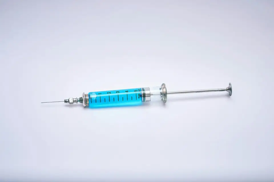 A medical syringe filled with blue liquid on a light background
