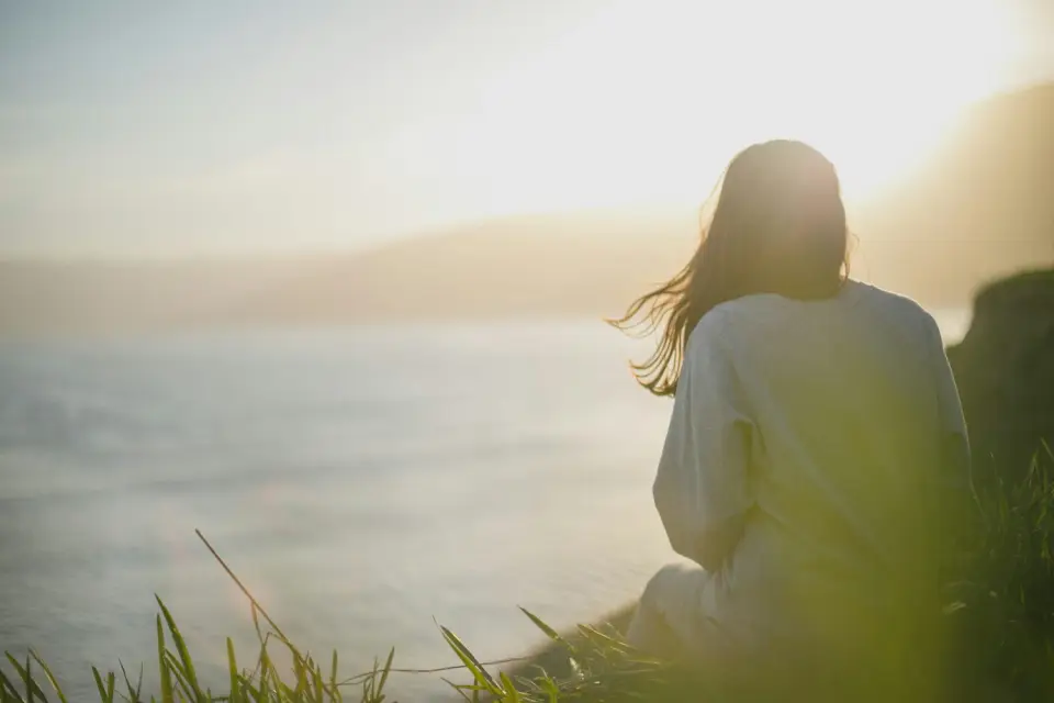 A woman resting outdoors at sunset, looking out over the water