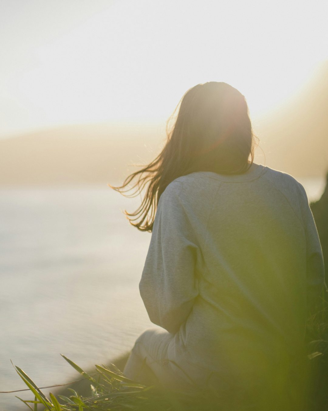 A woman resting outdoors at sunset, looking out over the water