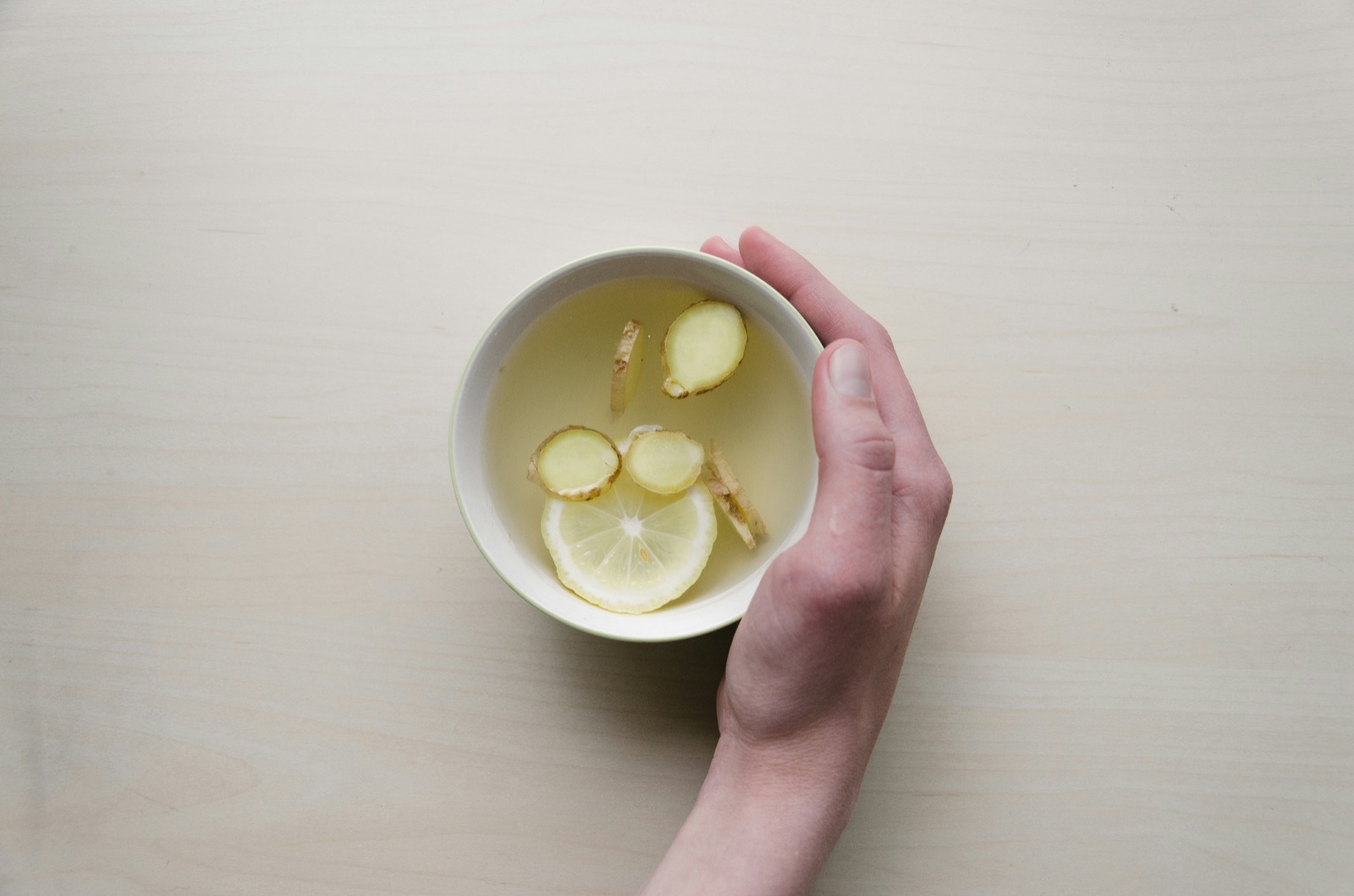 A hand cradling a bowl of ginger and lemon tea