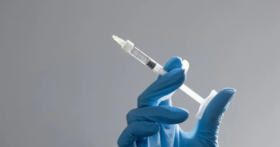 A gloved clinician's hand holding a prepared syringe in a clean clinical setting, representing physician-prescribed sermorelin dosing.