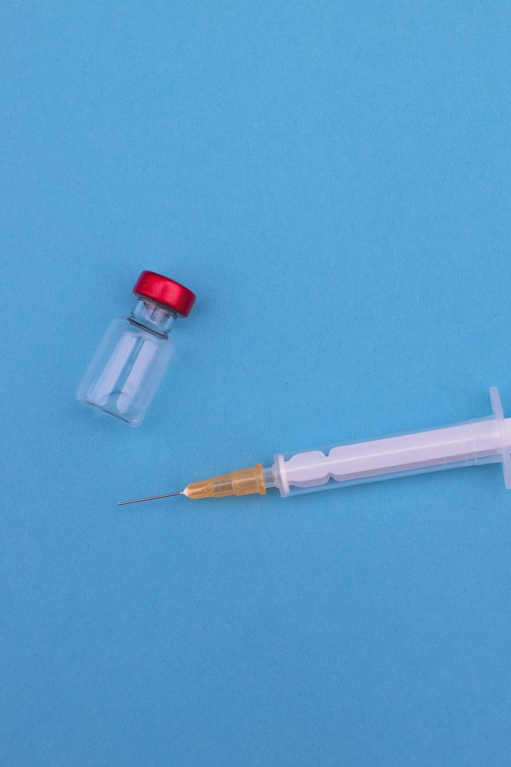 An unlabeled glass medication vial and a syringe on a blue background