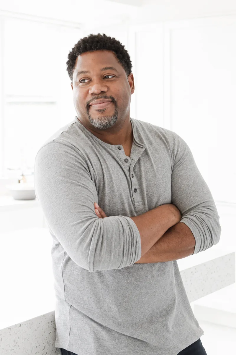 Man in a bright kitchen, arms folded, thinking it over