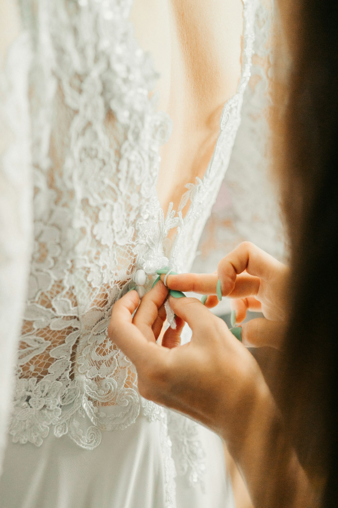 A bride's lace wedding dress being buttoned up the back before the ceremony