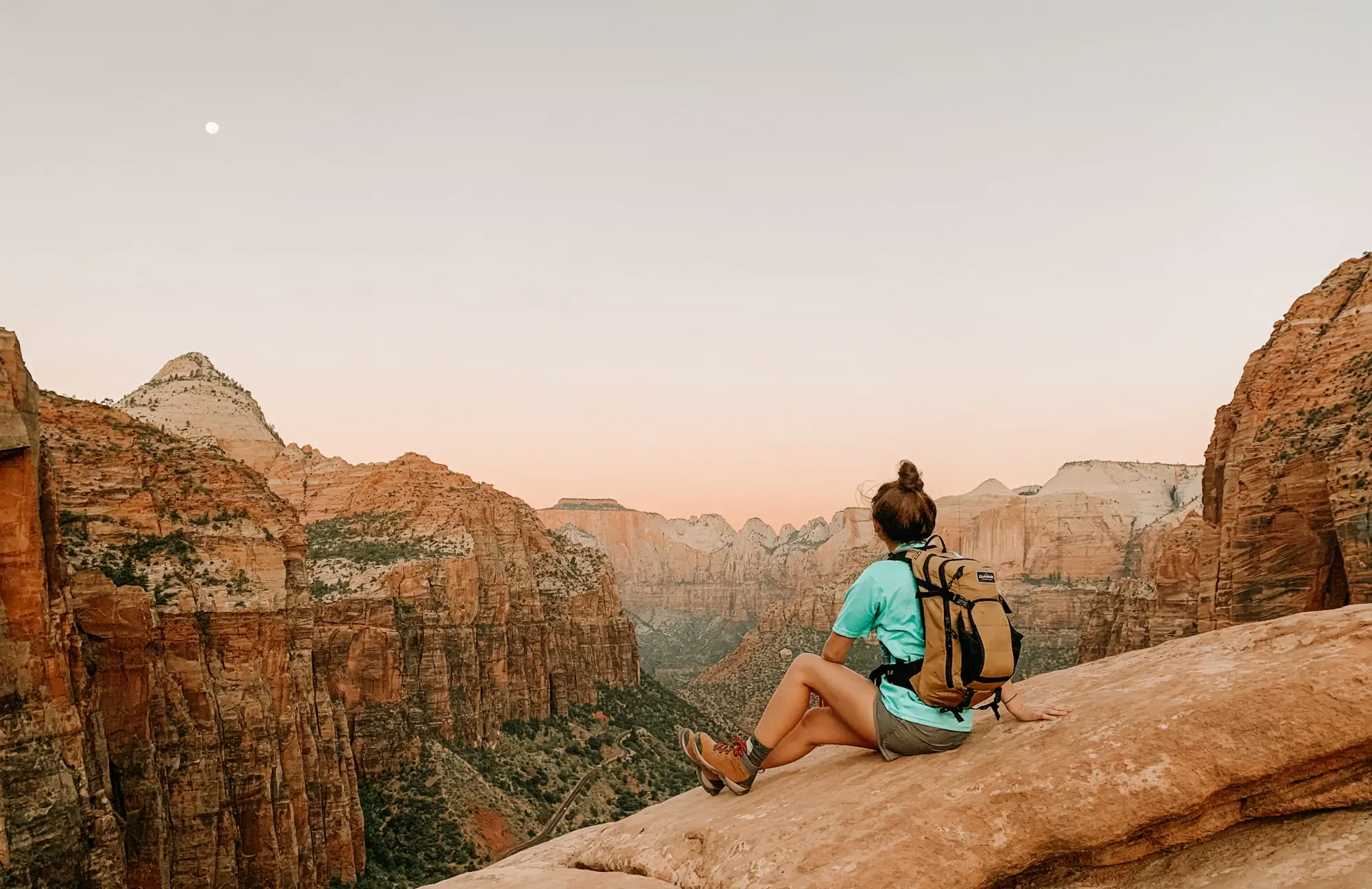 A woman on a mountain overlook taking in a canyon vista at sunrise