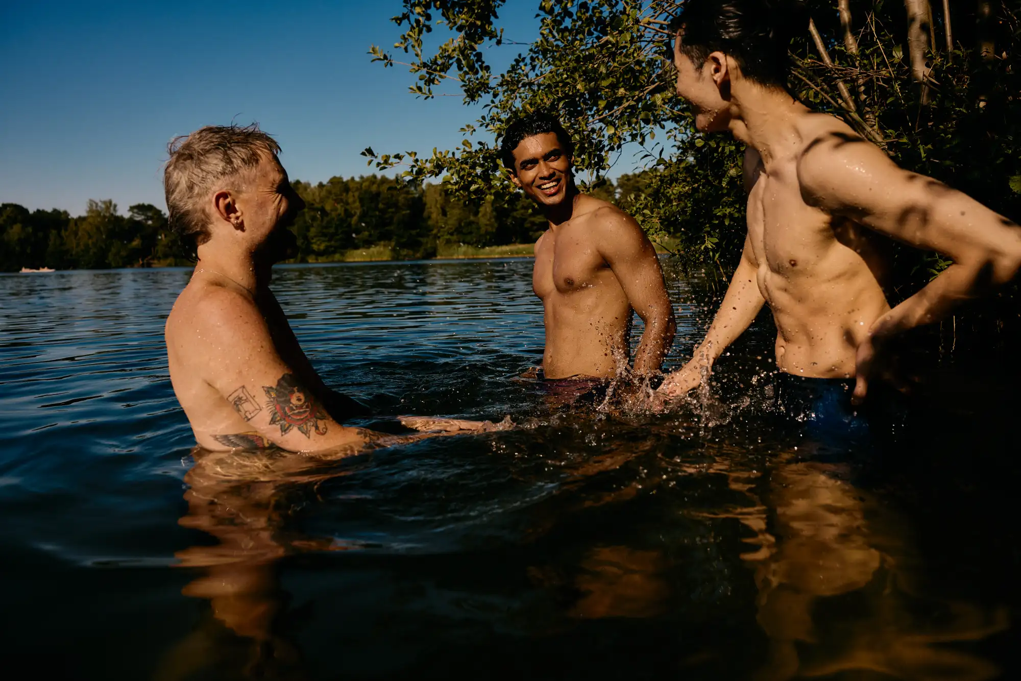 Three men laughing in a lake at golden hour